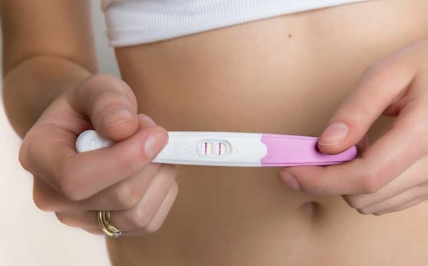 Lady holding a positive pregnancy test with two lines